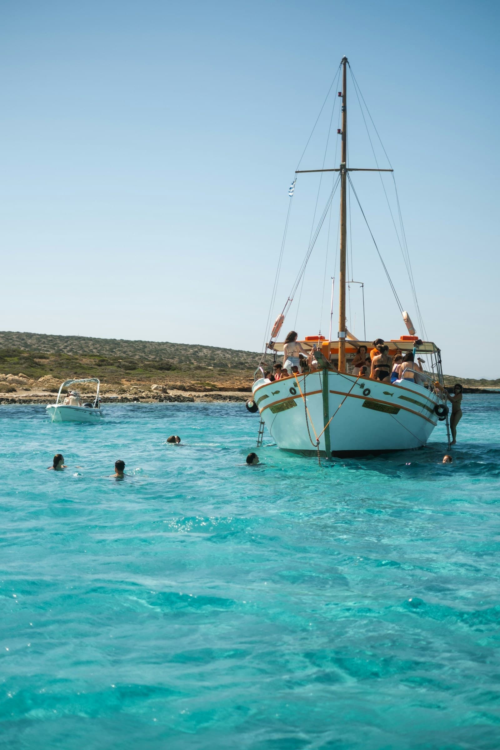 A traditional caique with guests on board, and swimmers in the clear turquoise water off Antiparos